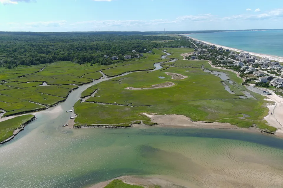 Coastal homes and a beach beyond green marshes and a winding inlet